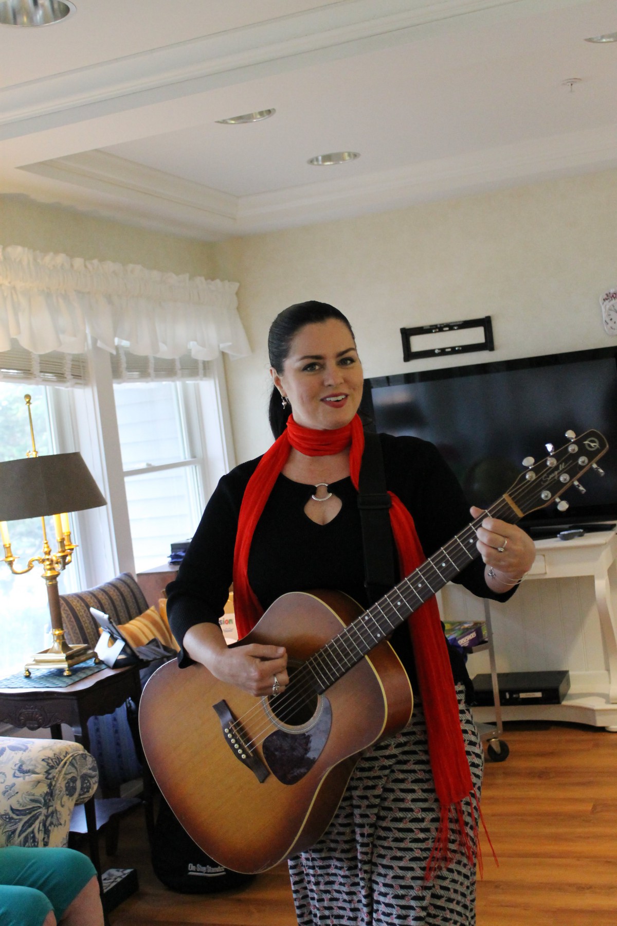 A woman playing the guitar indoors, wearing a red scarf.