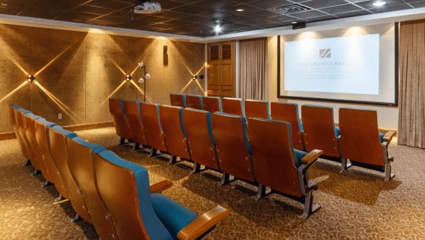 An empty theater room with rows of seats facing a large screen.