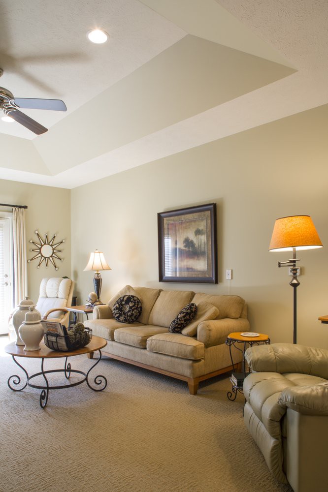 A cozy living room with neutral-toned furniture, including a sofa and armchairs, decorated with lamps and artwork.
