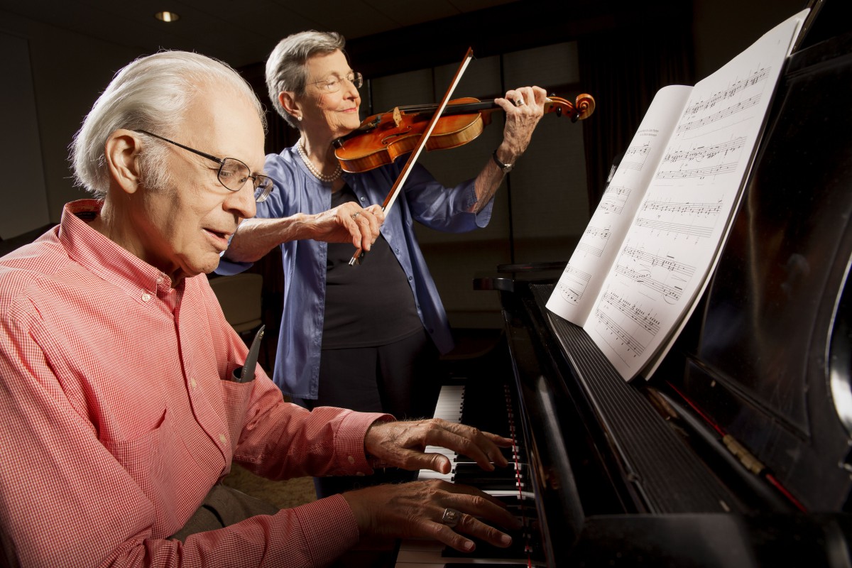 Two elderly musicians performing a duet with piano and violin.