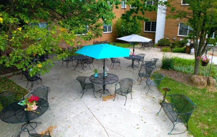 An outdoor patio area with tables, chairs, and umbrellas surrounded by greenery.
