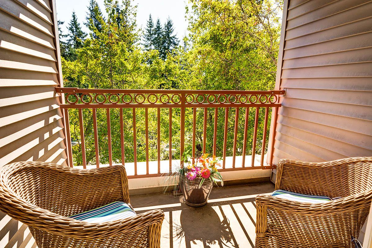 A sunny balcony with wicker chairs and a view of lush greenery.