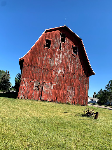 A weathered red barn standing tall against the clear blue sky, surrounded by lush green grass.