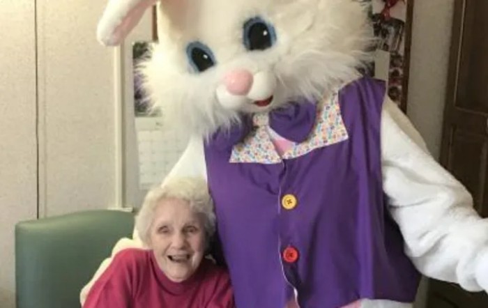 An elderly woman smiles while posing with a person in an Easter Bunny costume.