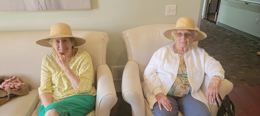 Two elderly women enjoying a moment together in their cozy chairs, both wearing stylish hats.