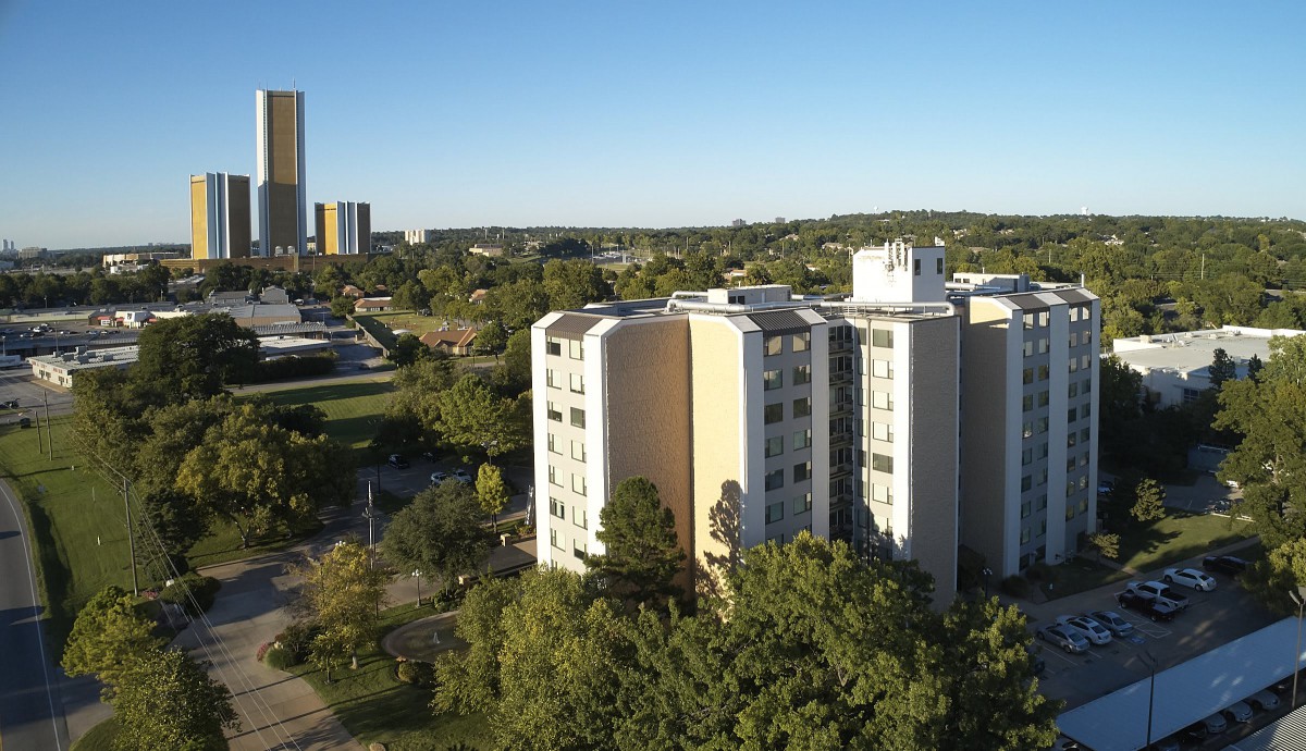A cityscape featuring tall buildings surrounded by trees under a clear blue sky.