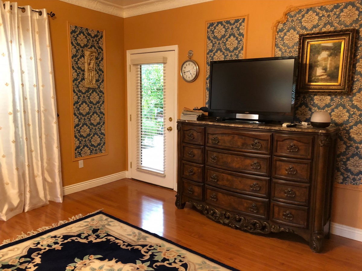 A cozy living room with orange walls, featuring a large wooden dresser and television, complemented by decorative wall art and a patterned rug.