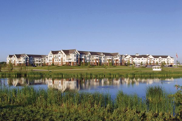 A row of residential buildings reflected in a calm body of water with a clear blue sky.