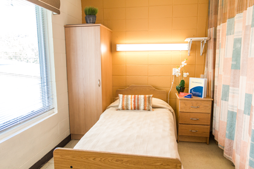 A cozy, minimalist hospital room featuring a single bed and wooden furniture.