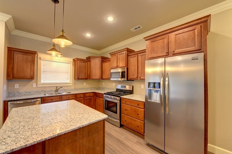 A modern kitchen with wooden cabinets, granite countertops, and stainless steel appliances.