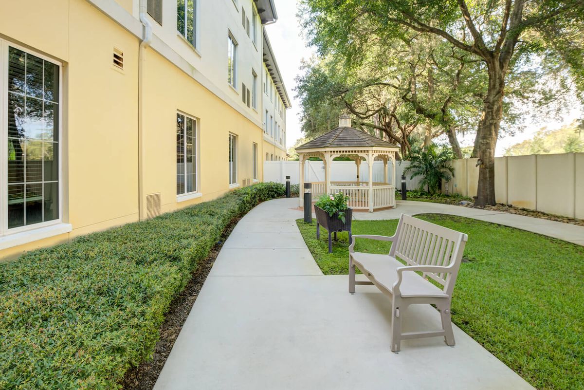 A peaceful outdoor setting featuring a bench, gazebo, and landscaped walkway beside a building.