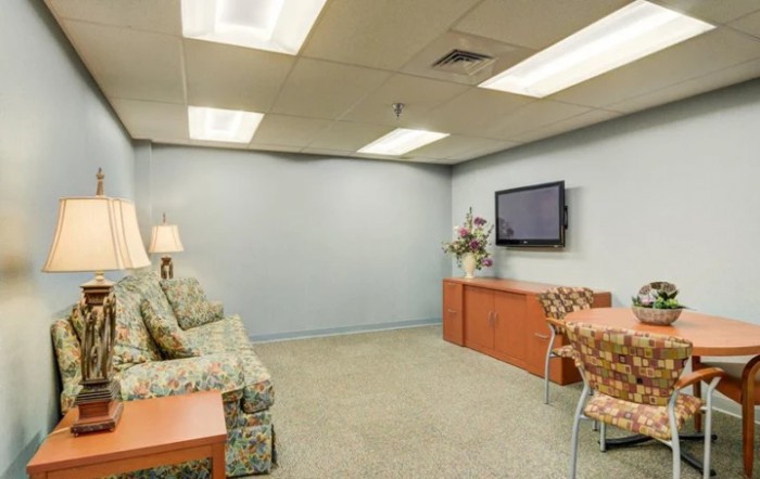 A cozy waiting room with a sofa, television, lamp, and decorative elements.