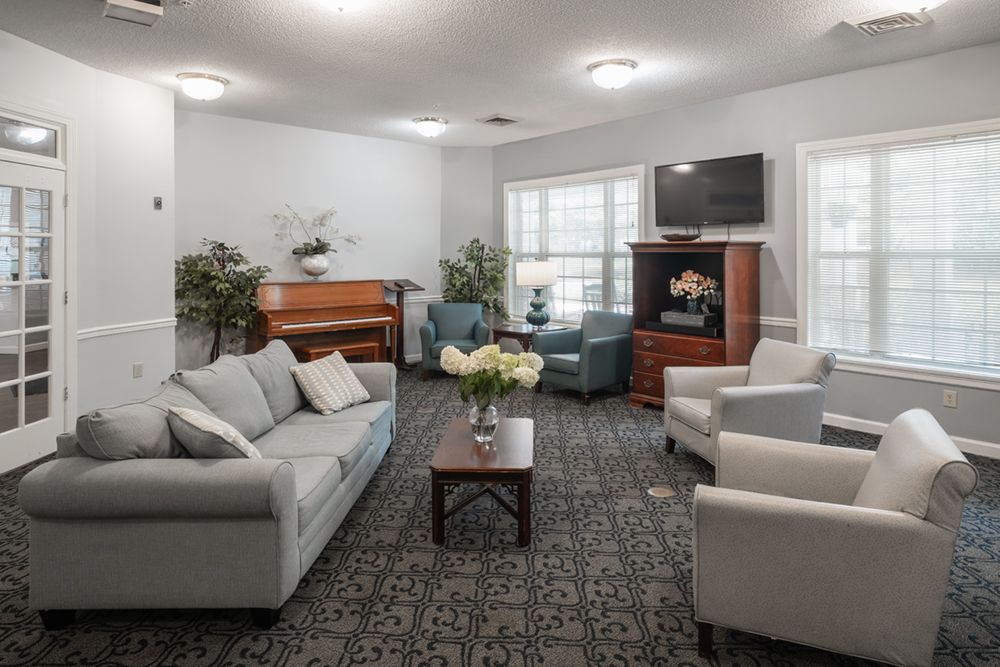 A cozy living room with sofas, armchairs, a piano, and a television.
