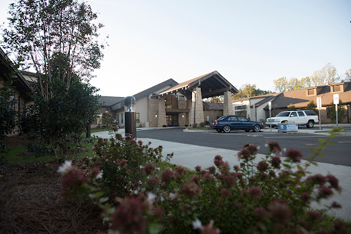 A modern architectural building surrounded by landscaped flowers and a parking area.