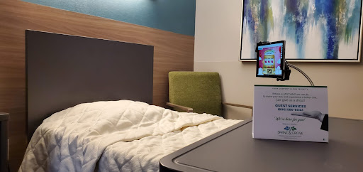 A cozy hotel room featuring a neatly made bed, a green chair, and a workspace with a screen.