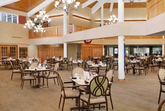 An empty dining room with neatly arranged tables and chairs, featuring elegant chandeliers.