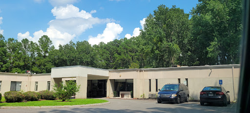 A modern building surrounded by greenery under a bright blue sky.