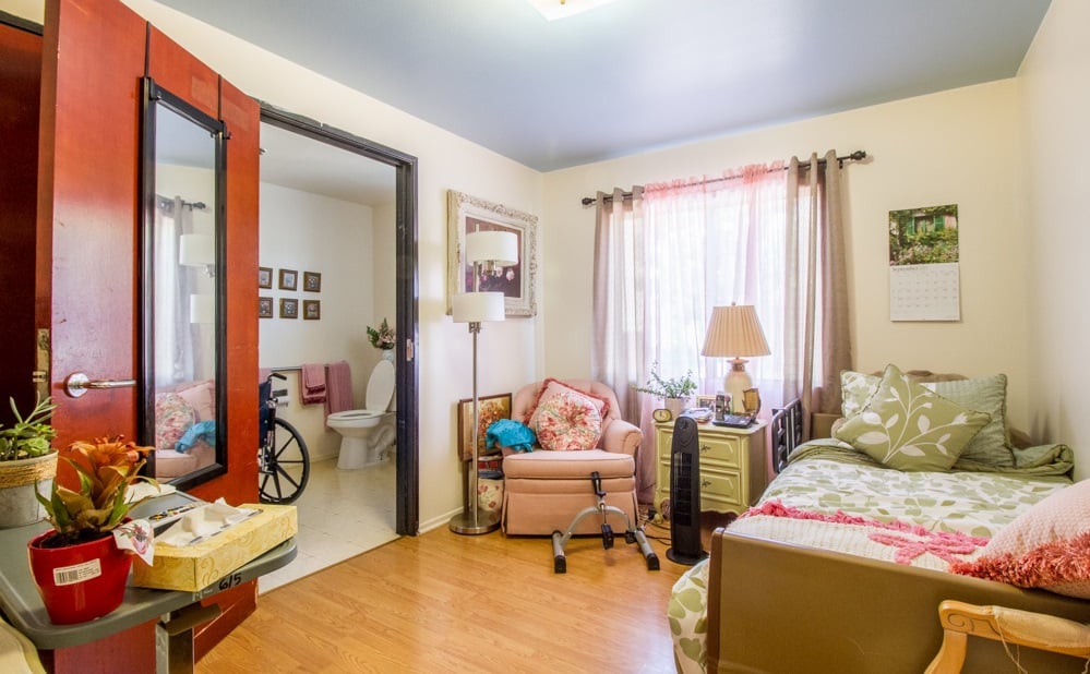 A cozy living space featuring a comfortable chair, bed, and a lamp by the window with soft lighting.