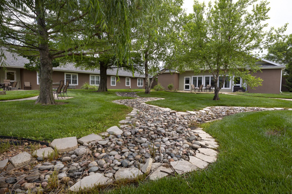 A tranquil garden with a winding rock path and lush greenery near a house.