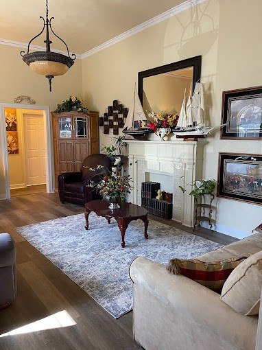 A cozy living room with nautical-themed decor, featuring a large mirror above the fireplace and plush seating around a coffee table.