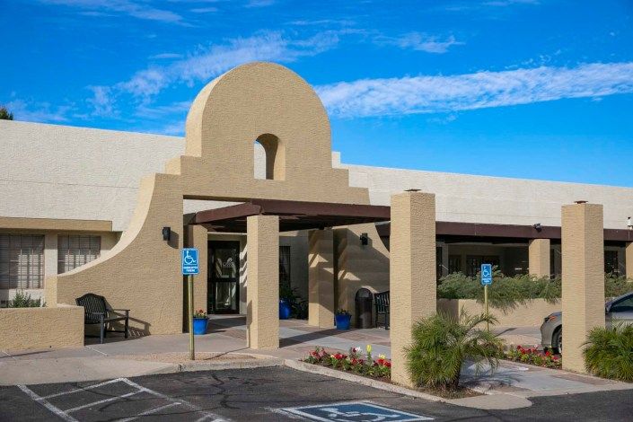 The entrance to a building featuring desert-style architecture with a parking lot and handicap spaces.