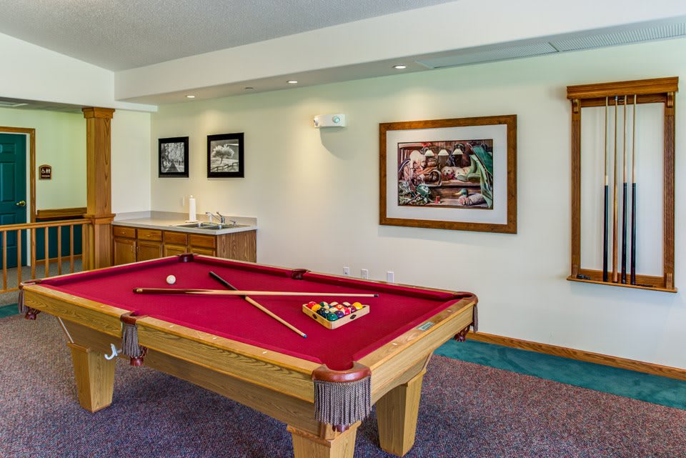 A cozy billiard room featuring a pool table with red felt, cue sticks, and framed artwork on the walls.
