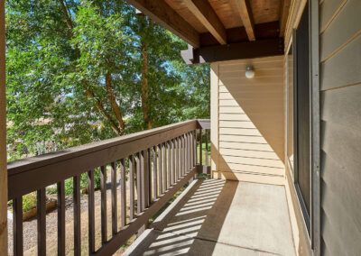 A sunny balcony with wooden railings overlooking trees.