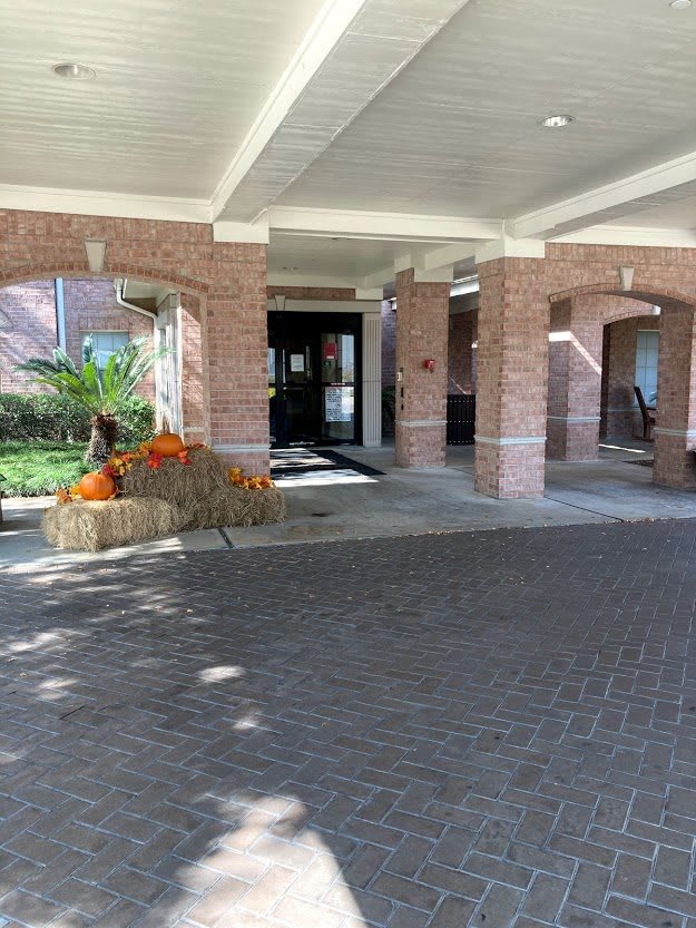 The entrance to a building features pumpkins and hay bales as seasonal decorations under a covered walkway.