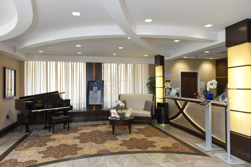 A modern hotel lobby featuring a reception desk, seating area, and grand piano.