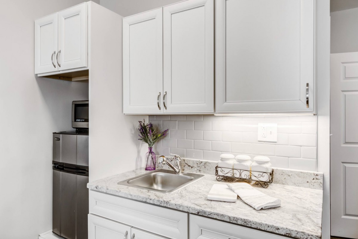 A modern kitchen with white cabinets and a marble countertop, featuring a sink and decorative elements.
