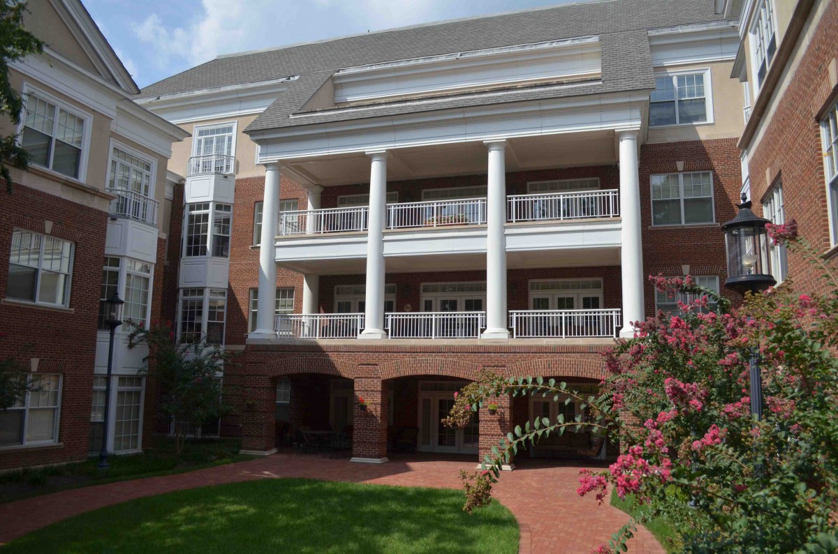 A large brick building with white columns and balconies surrounded by a garden.
