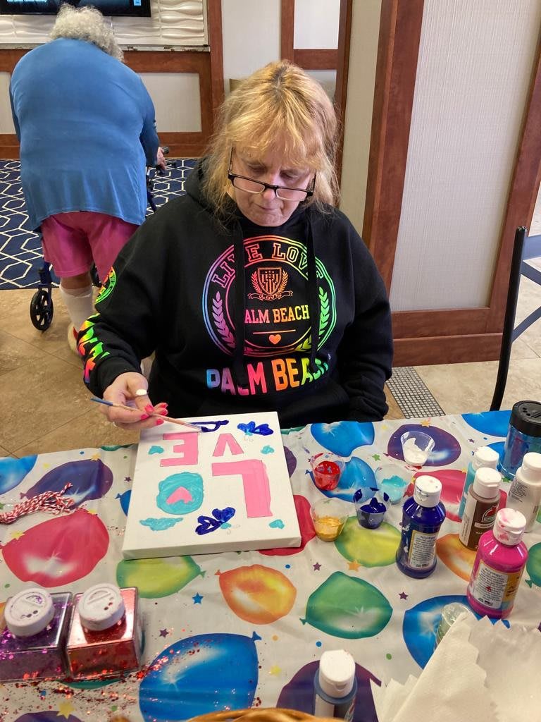 A woman painting a colorful canvas at a craft table.