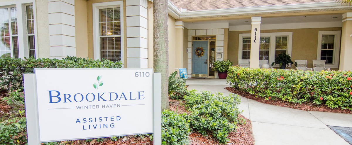 Entrance of a residential building with a sign, surrounded by greenery and well-maintained landscaping.