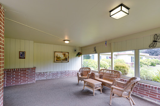 A cozy indoor porch featuring wicker furniture and large windows, perfect for relaxation.