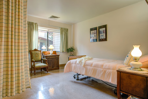 A serene hospital room featuring a bed, chairs, and natural light from the window.