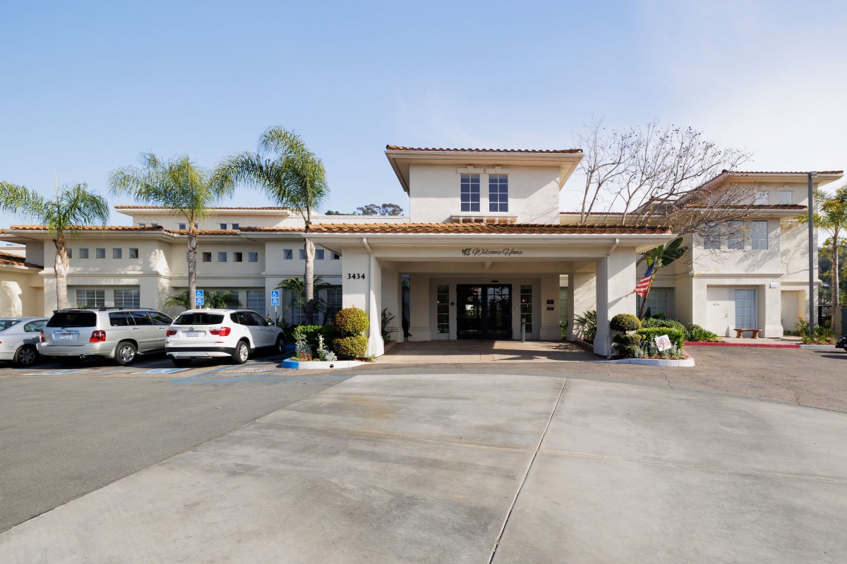 A building entrance with parking and palm trees nearby.