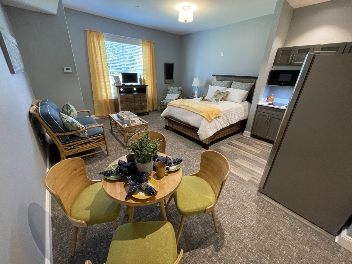 A cozy studio apartment featuring a bed, a seating area, and a dining table.