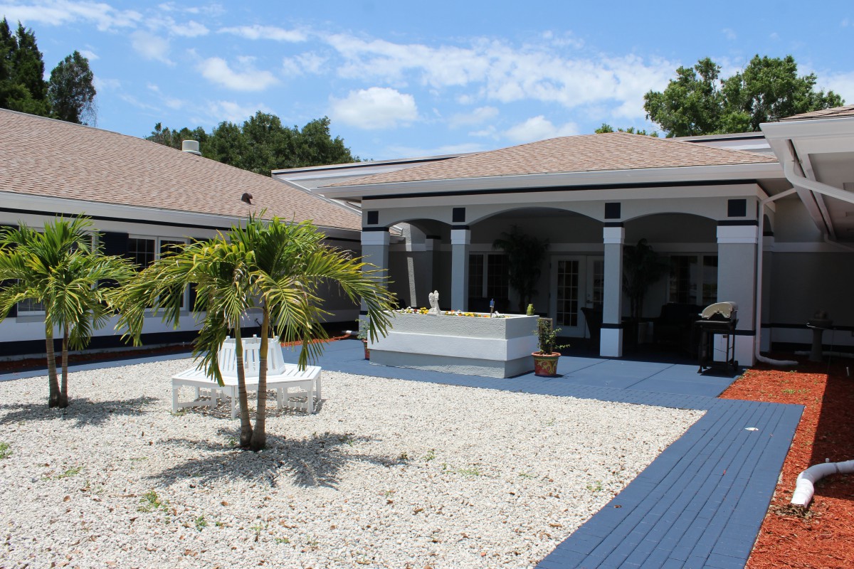 A spacious courtyard featuring a palm tree and outdoor seating, surrounded by a single-story house with archways.