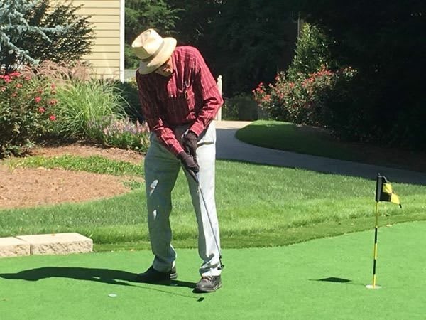An elderly person putting on a golf green on a sunny day.