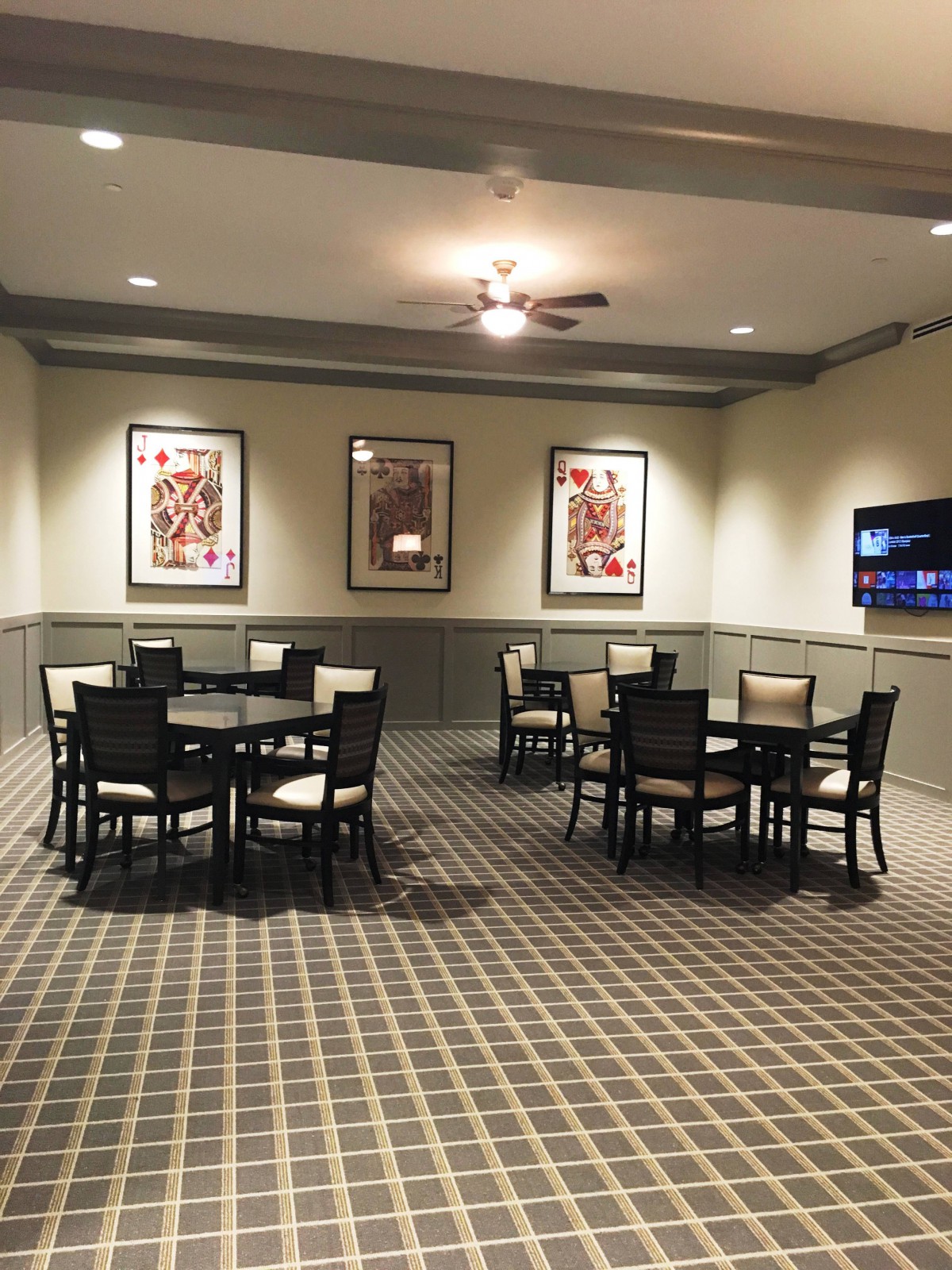 A neatly arranged room with tables and chairs, featuring framed artwork on the walls and a checkered carpet.