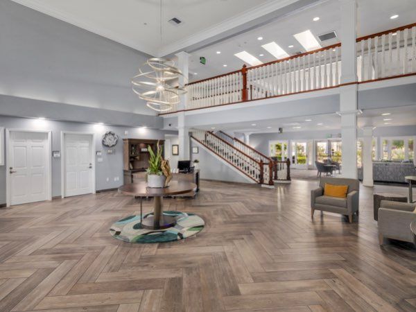 A spacious and modern lobby with elegant wood flooring and a central chandelier, featuring comfortable seating and a prominent staircase.