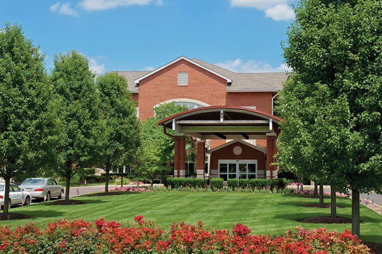 A red brick building surrounded by lush green trees and a manicured lawn under a partly cloudy sky.