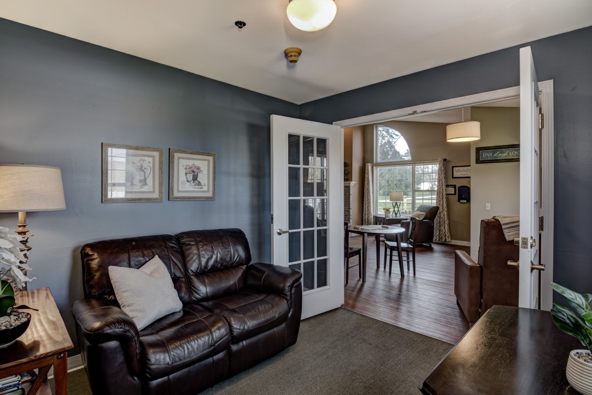 A cozy living room with a leather sofa and a view into the dining area through French doors.