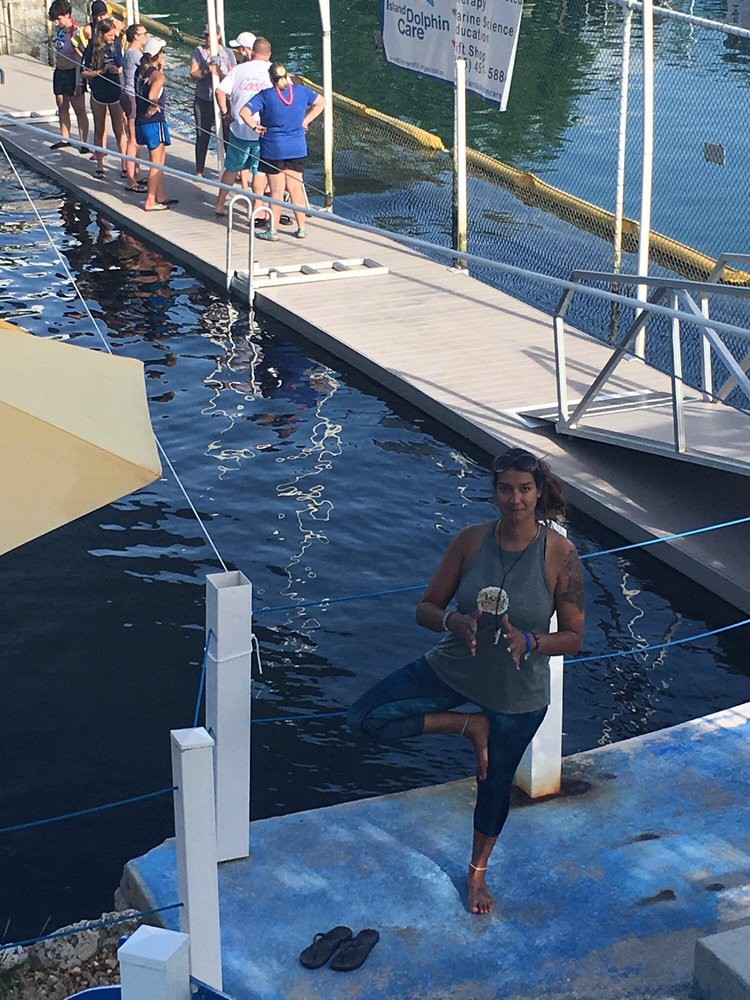 A person standing on a dock near the water, with a group of people in the background enjoying the day.