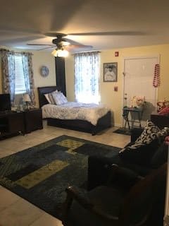 A cozy studio apartment with a combined bedroom and living area, featuring a bed, sofa, television, and decorative rug.