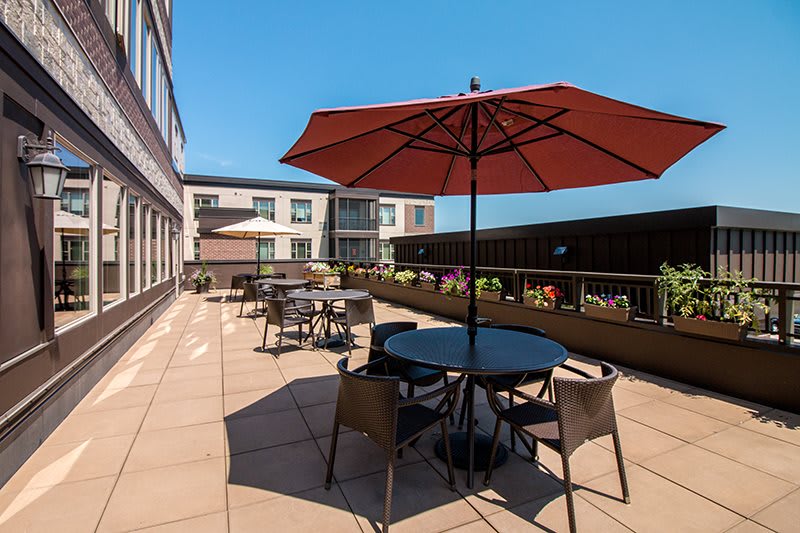 A sunny outdoor patio with tables, chairs, and umbrellas on a terrace next to a building.