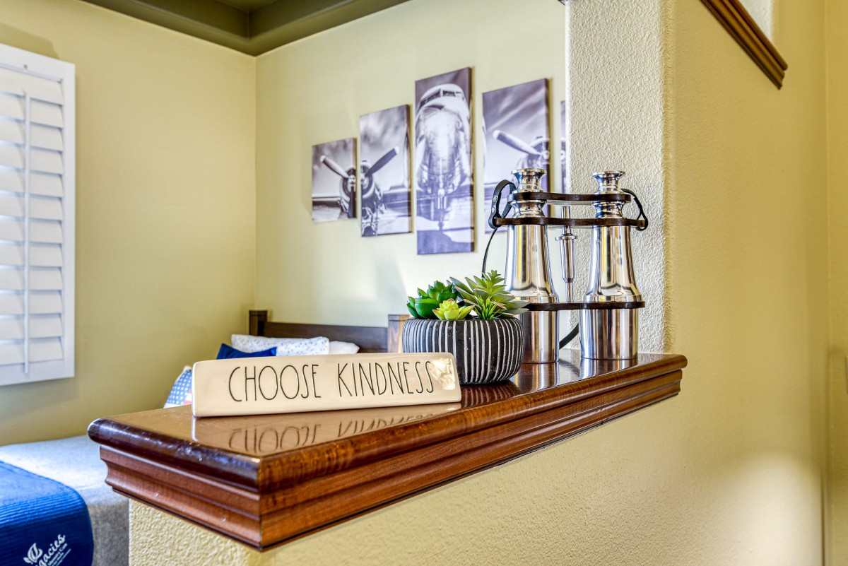 A cozy corner with a shelf displaying plants, artwork, and a sign reading 'Choose Kindness'.
