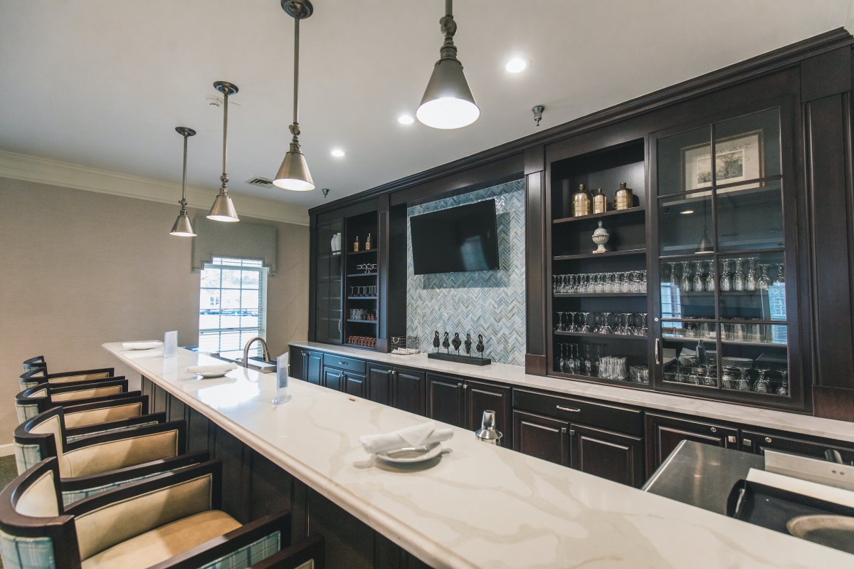 A modern bar interior featuring a long marble counter, pendant lighting, and a built-in television.