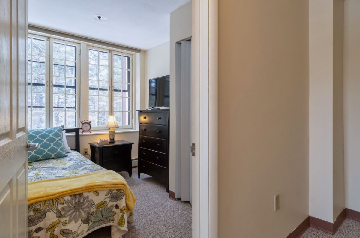 A cozy bedroom with a bed, nightstand, and dresser by the window.