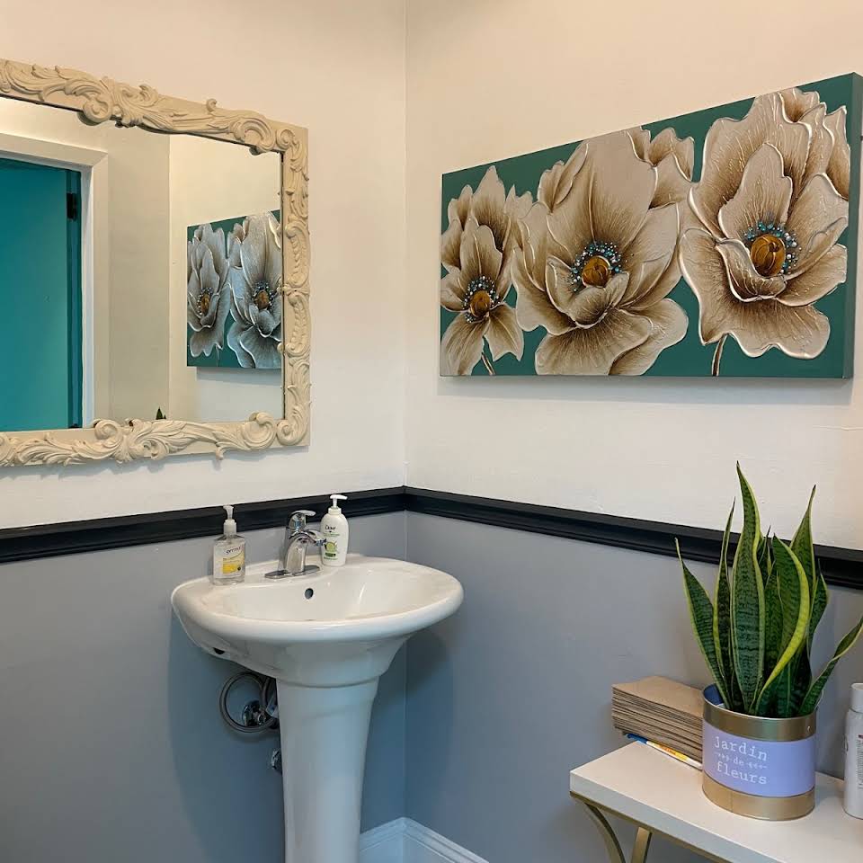 A well-decorated bathroom with a pedestal sink, large mirror, and floral artwork on the wall.